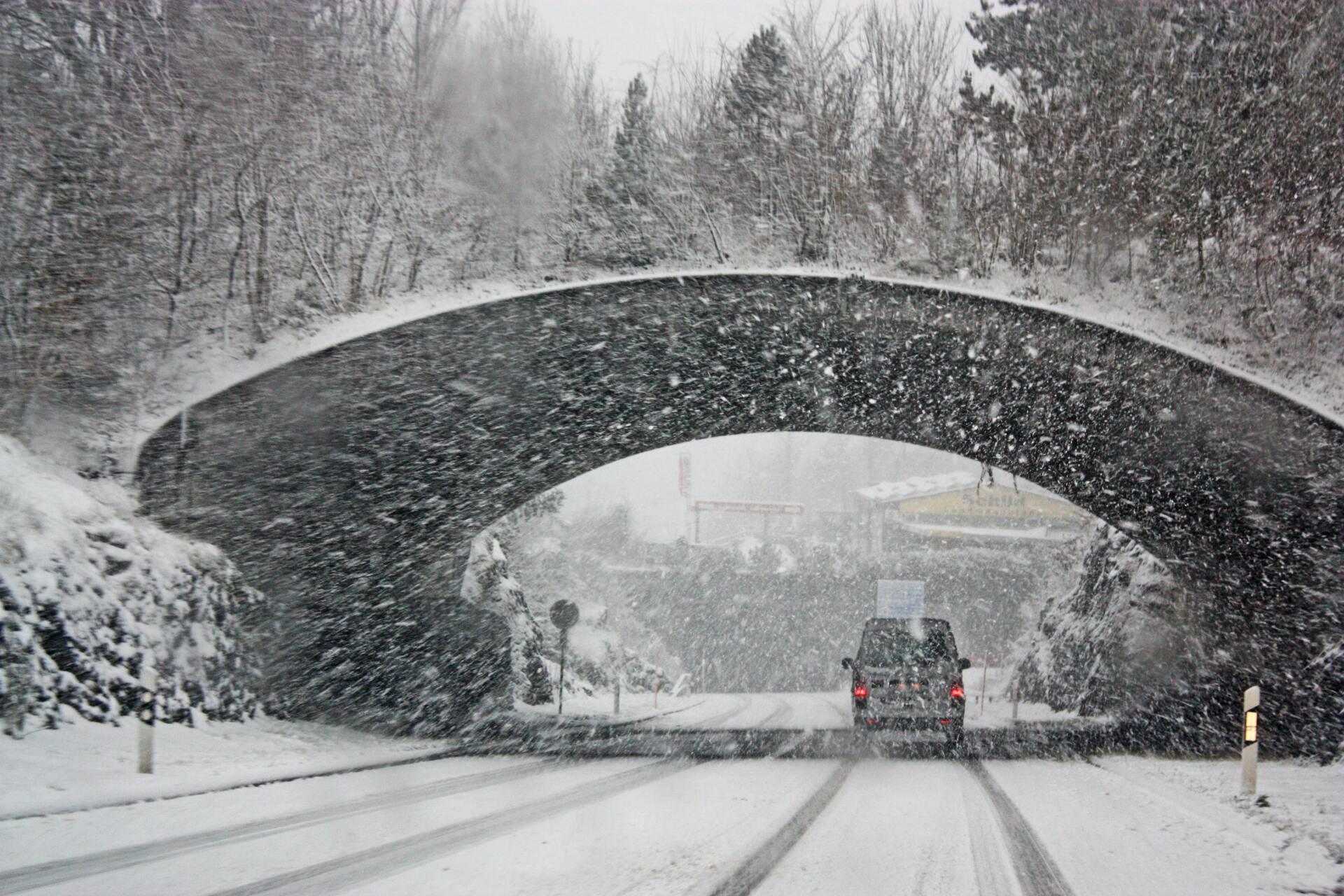 A car drives on a snow-covered road during heavy snowfall