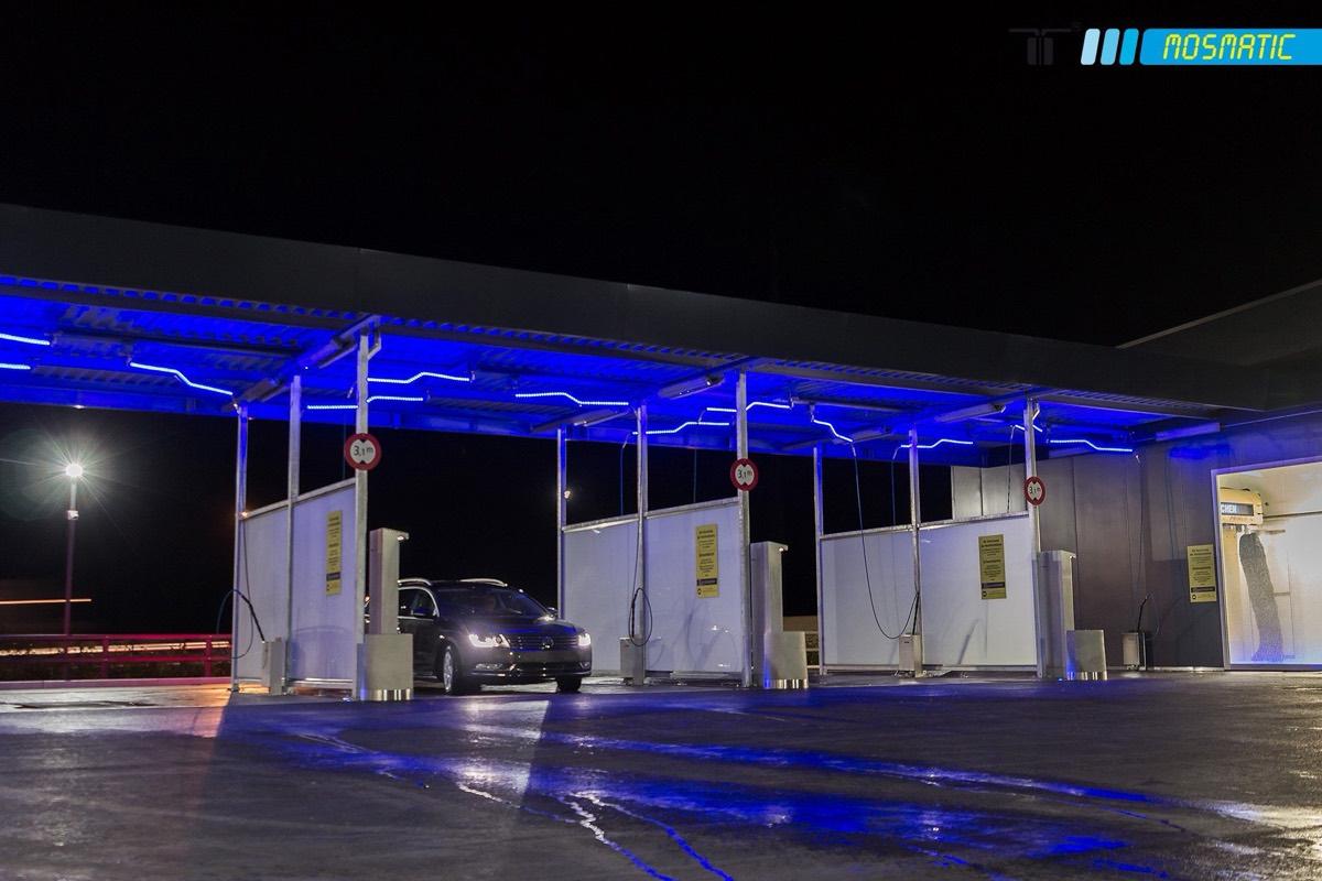 Overhead car wash boom with LED lighting and hoses mounted in a wash bay.